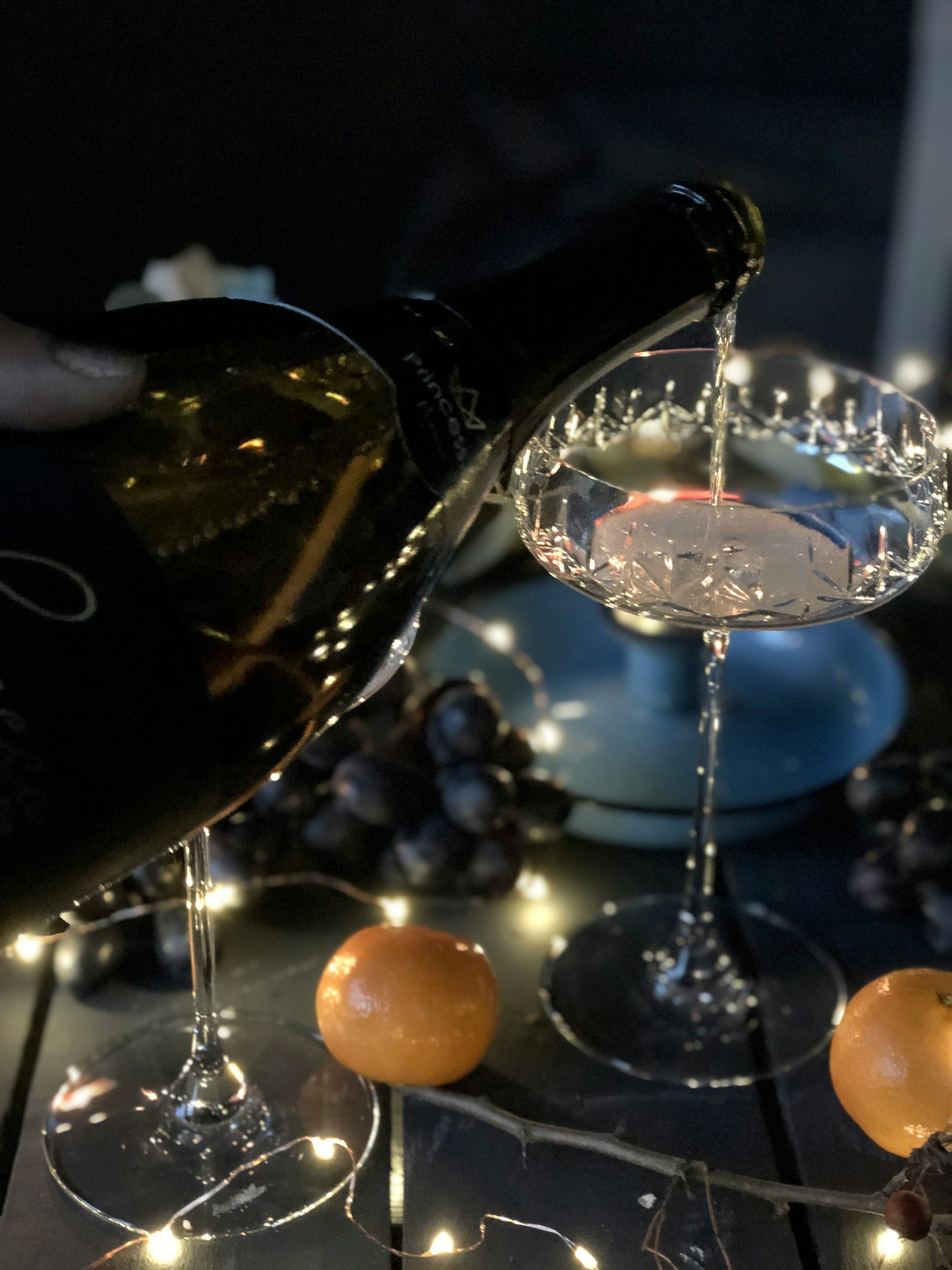 Bottle of champagne being poured into a glass with decorative elements and lights in the background