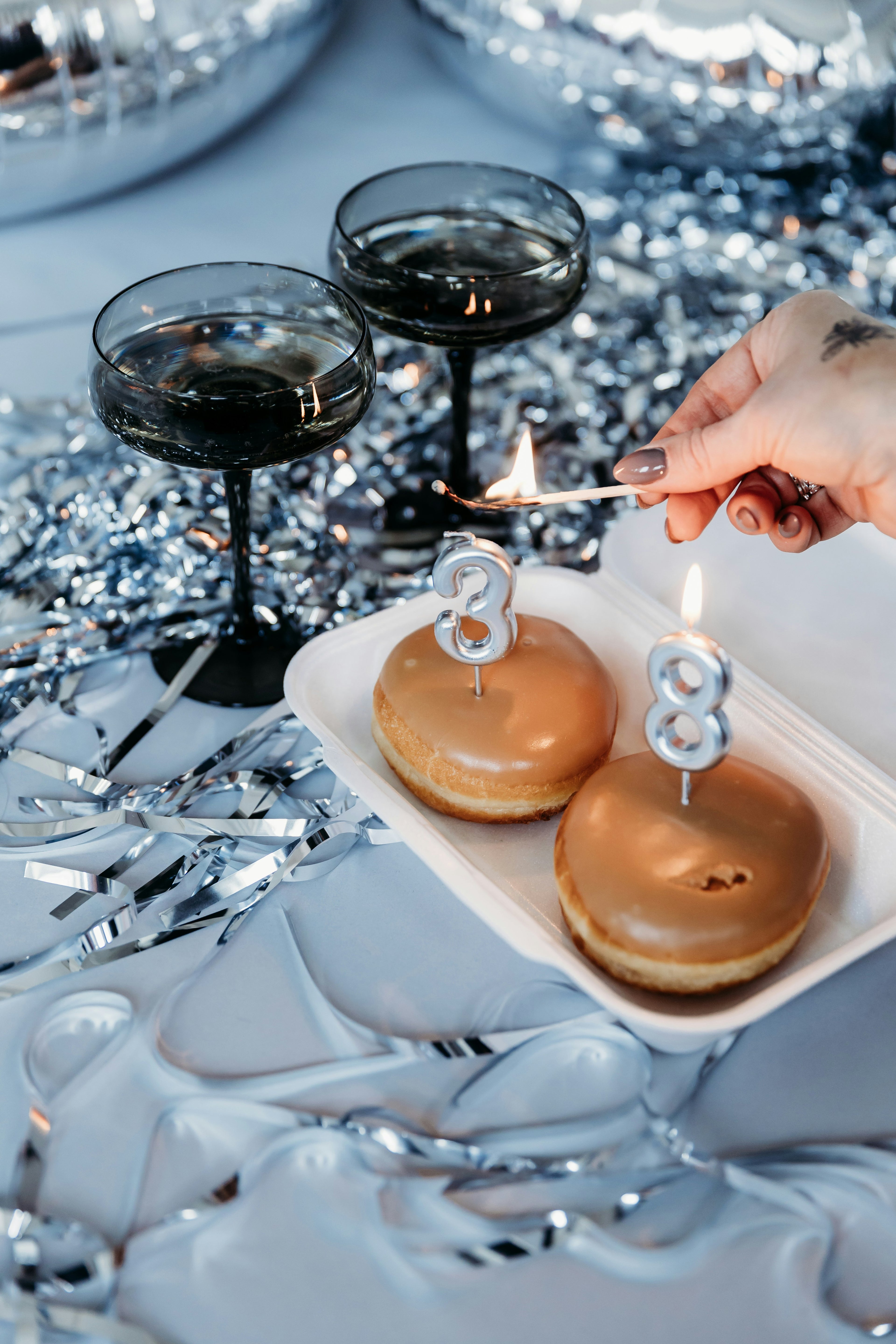 Two donuts with candles shaped like the number 38 on a tray, with two black cocktails in the background.